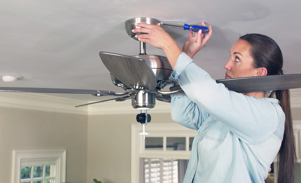 A person detaches the ceiling fan canopy from the ceiling bracket.