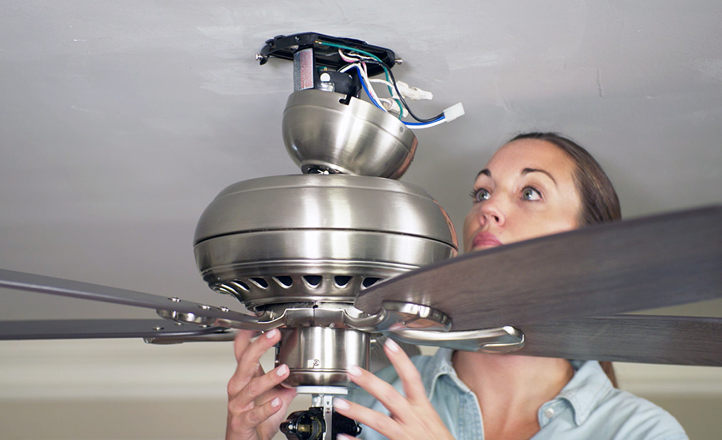 A person detaches a flushmount ceiling fan from the ceiling bracket.