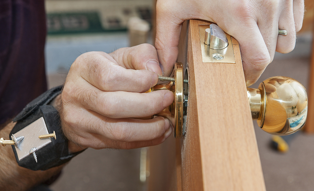 A person removing a screw from a door knob.