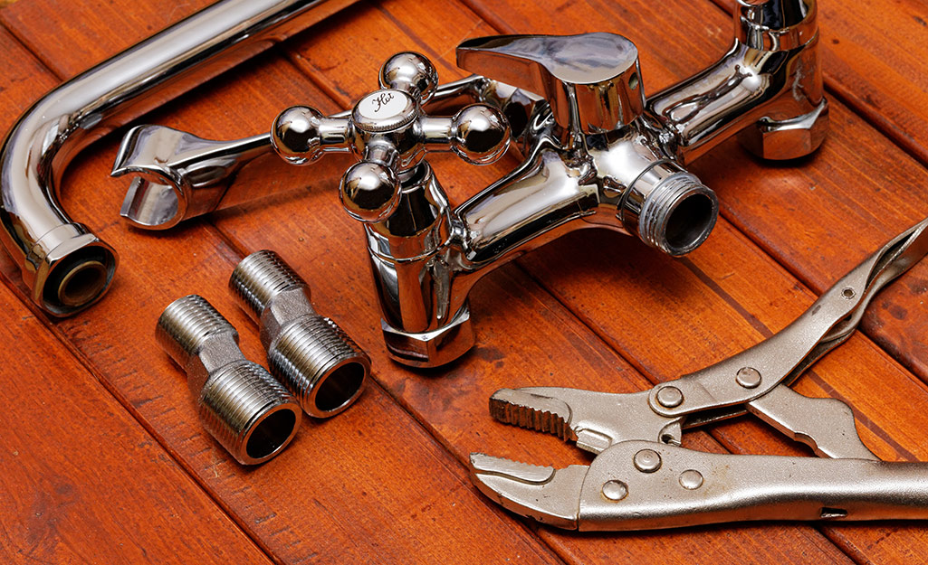 Wrenches, faucet and other plumbing items on a wood table.