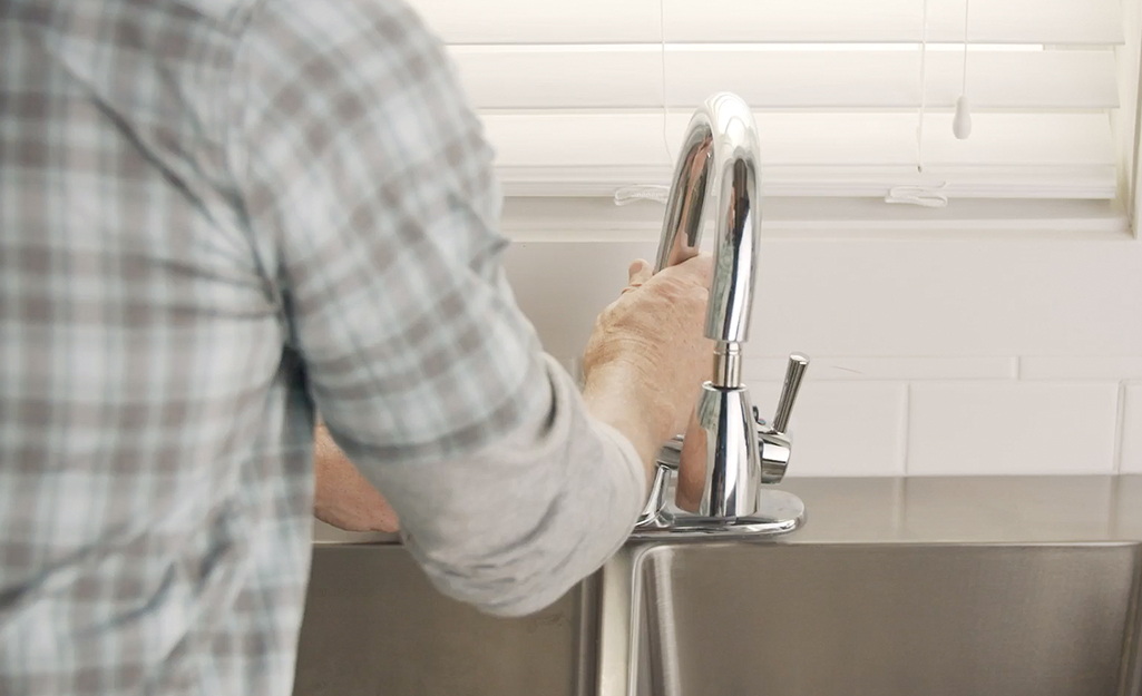 Someone pulling a kitchen faucet from a sink.