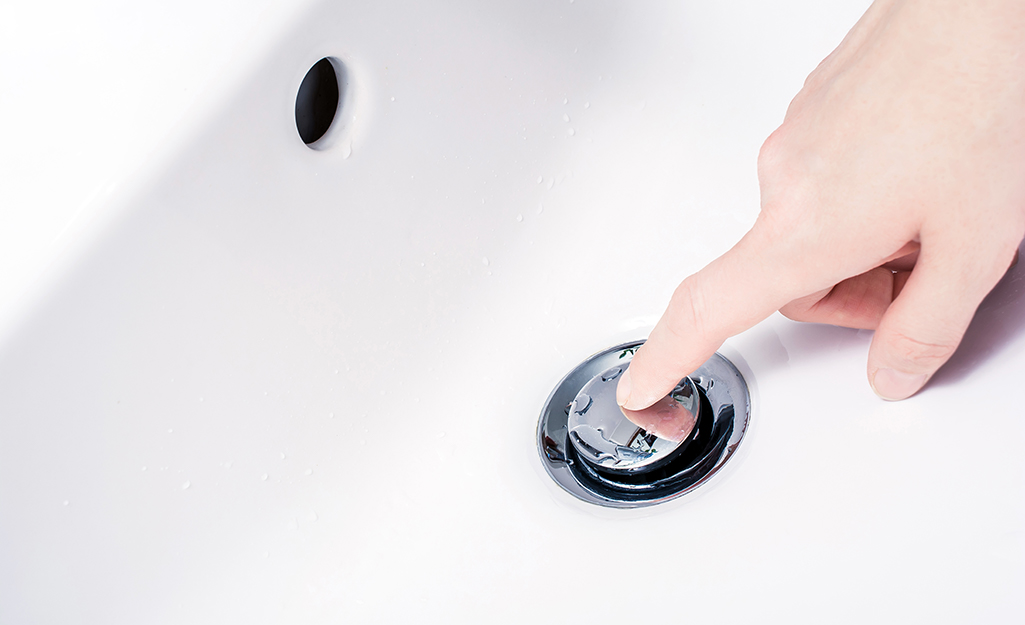 Person pushing down a sink stopper.