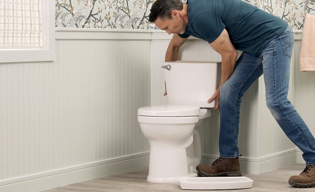 A person removing a toilet tank from the toilet basin.