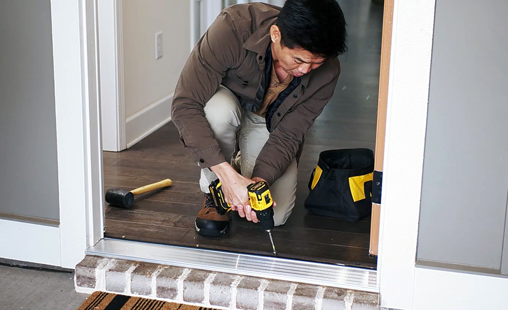A person uses a power drill to install a metal threshold.