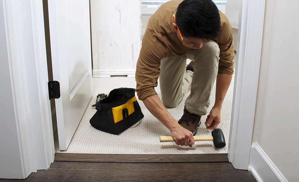 A person uses a mallet to tap an interior threshold into place.
