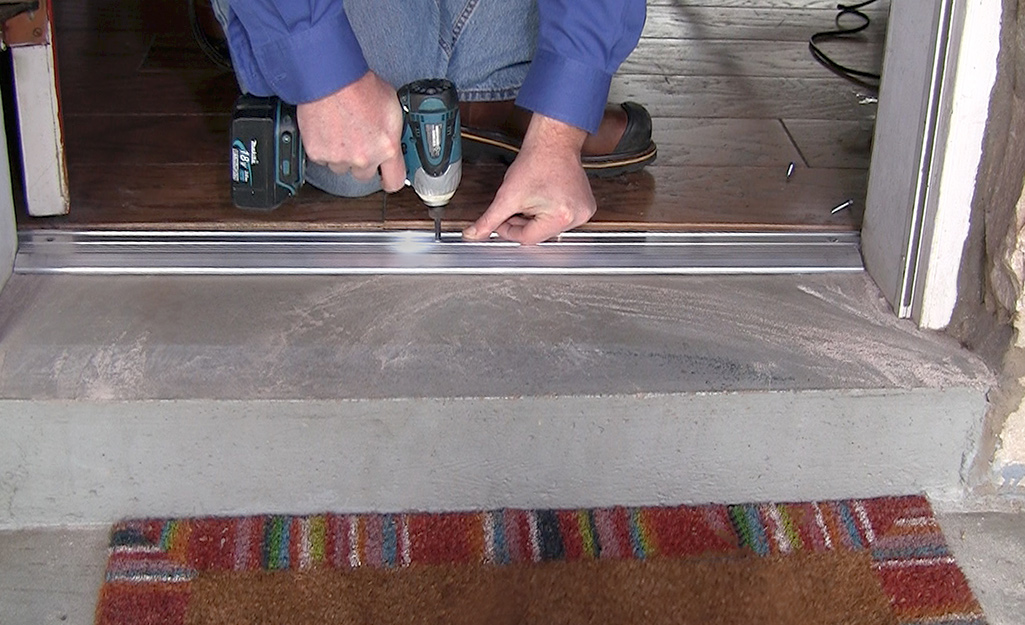 A person uses a power drill to install a metal threshold. A person uses a power drill to install a metal threshold.