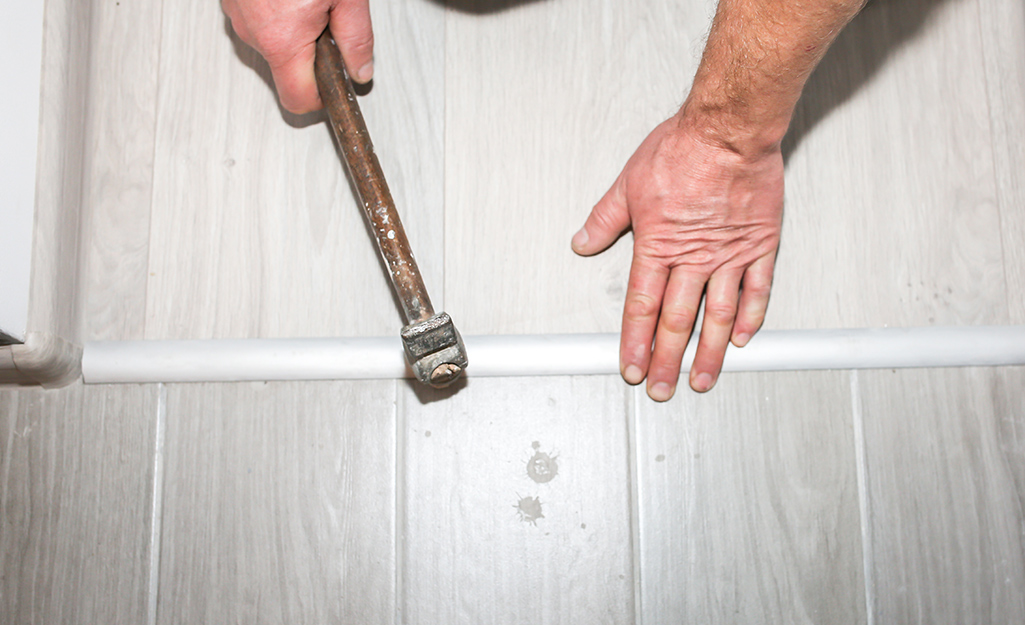 A person uses a hammer to tap an interior threshold into place. A person uses a hammer to tap an interior threshold into place.