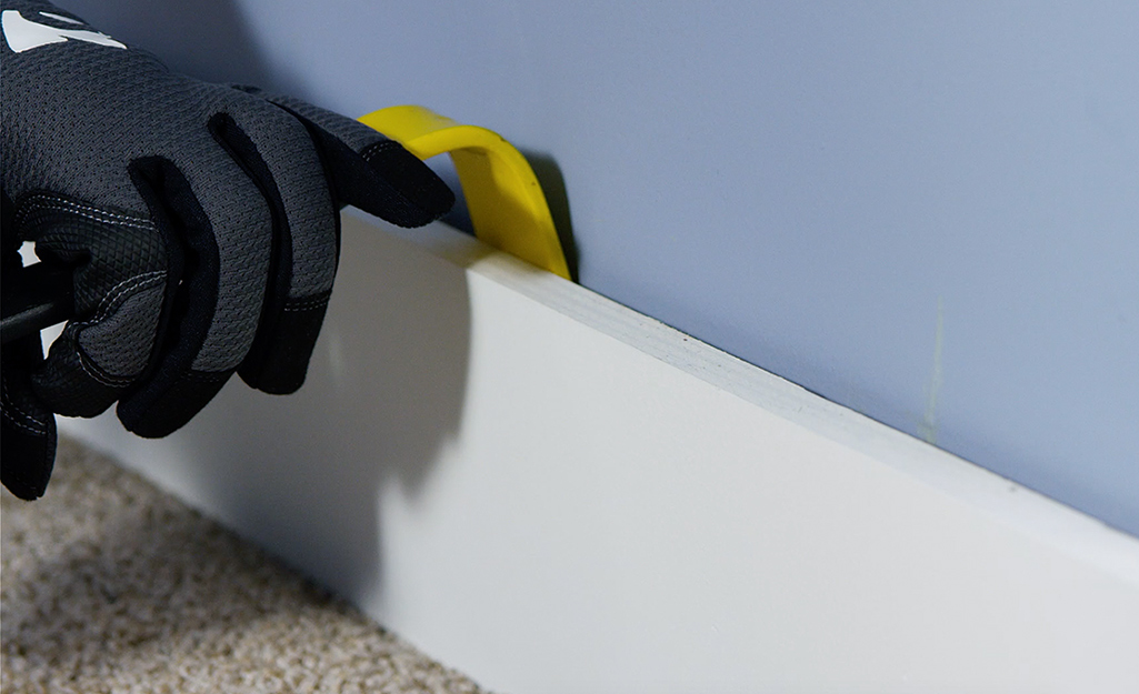 A person removing a baseboard with a pry bar.