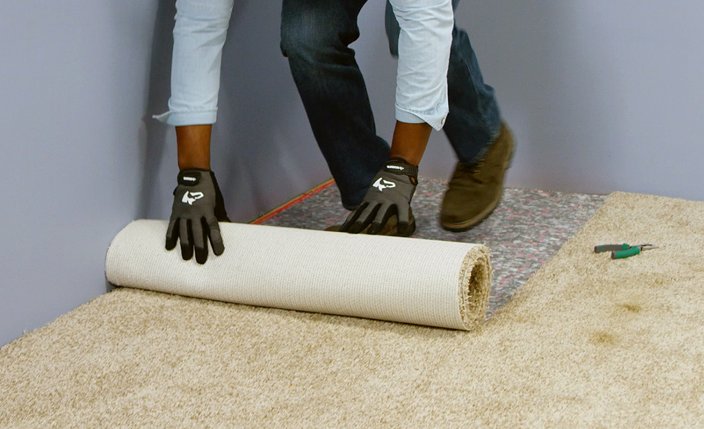 A person removing and rolling up a strip of carpet.