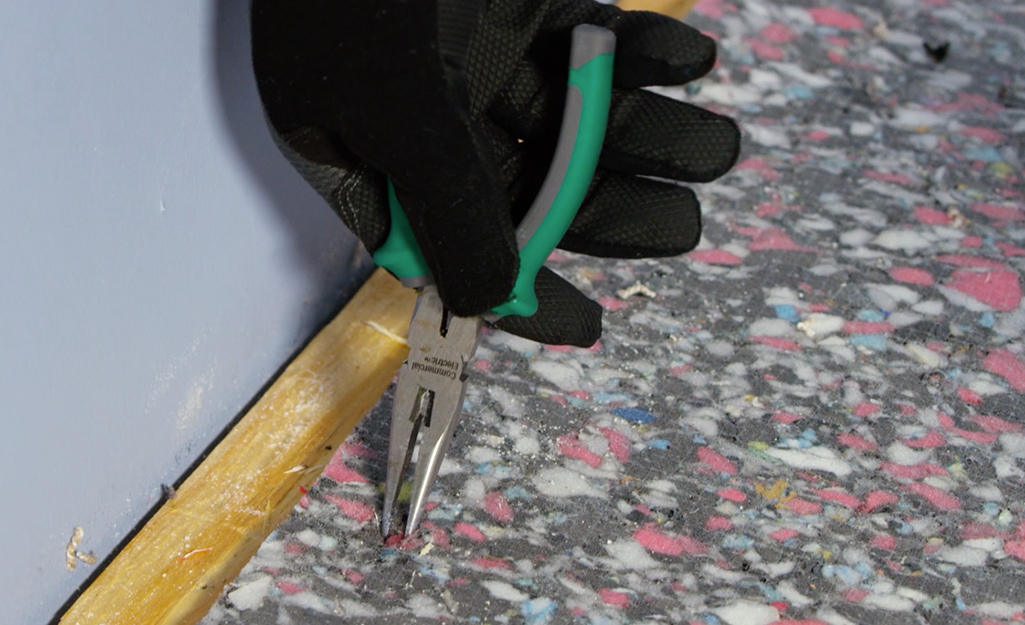 A person using pliers to remove carpet staples from old carpet padding.