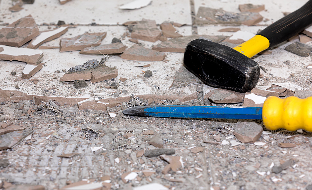 A peen hammer and chisel lying on broken tile.