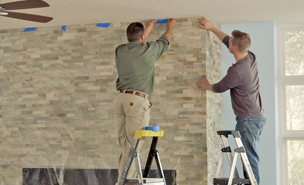 Friends applying painter's tape around a fireplace.