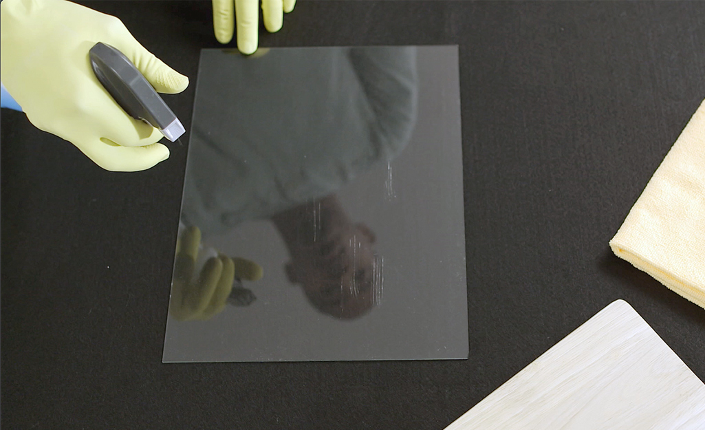 Person wearing yellow rubber gloves sprays glass cleaner on a window.