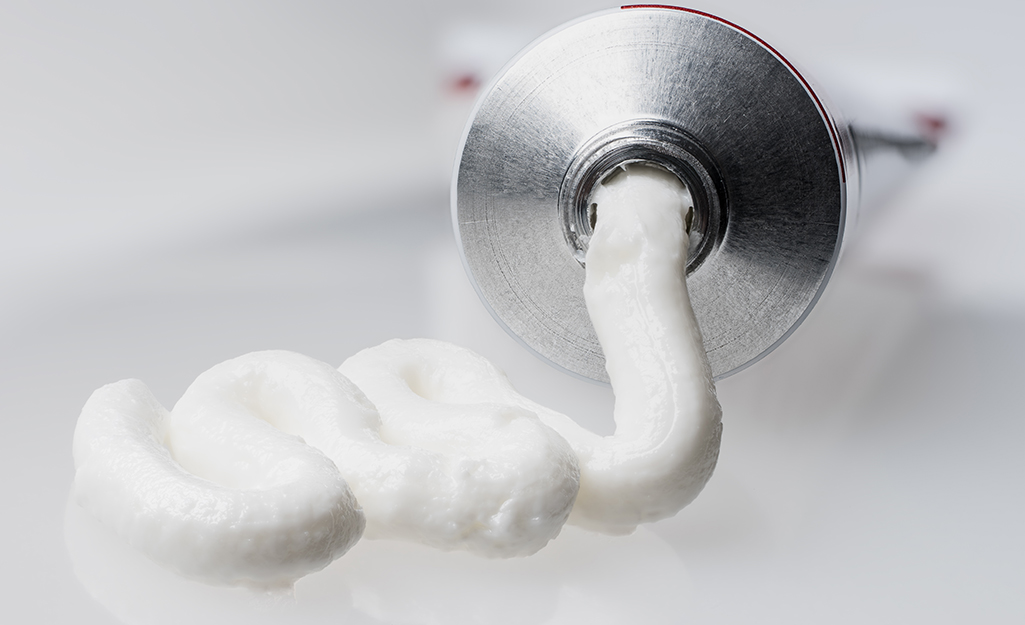 White toothpaste squeezes out of silver tube.