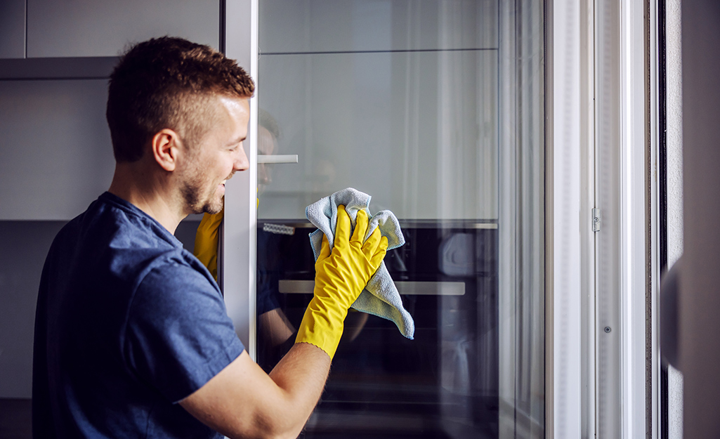 Man wearing yellow rubber glove smiles as he cleans a glass window with cloth.