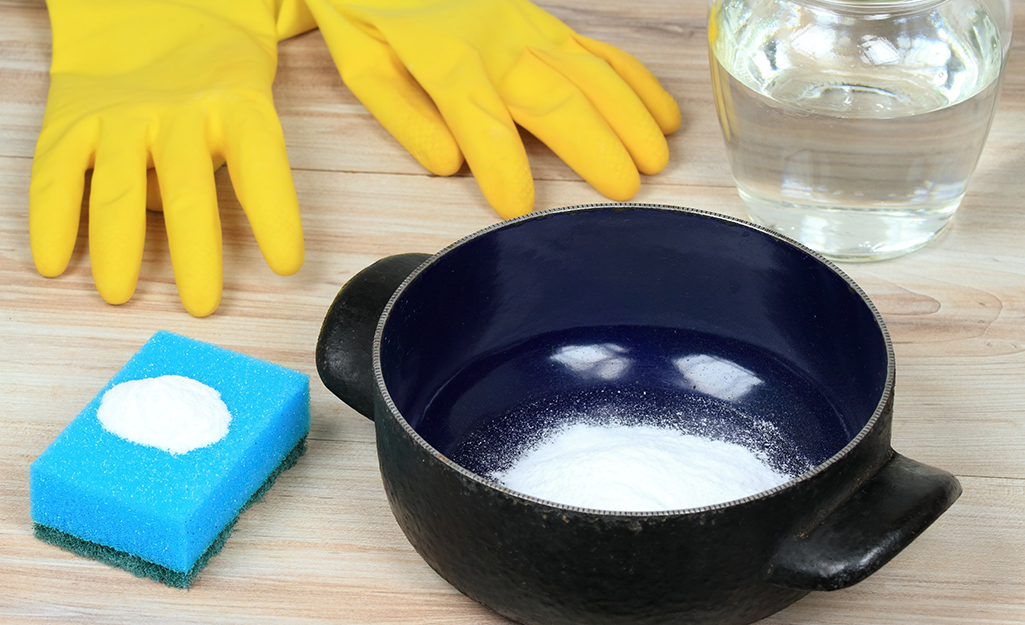 Yellow rubber gloves, a sponge and baking soda in a pot sit next to a glass container of water.