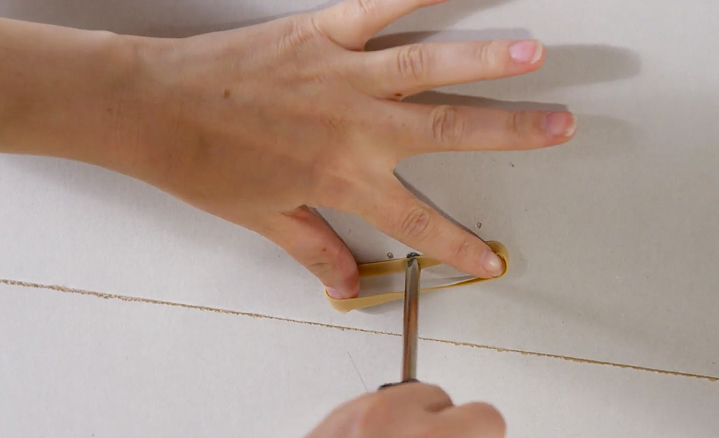 Someone using a rubber band to unscrew a stripped screw.