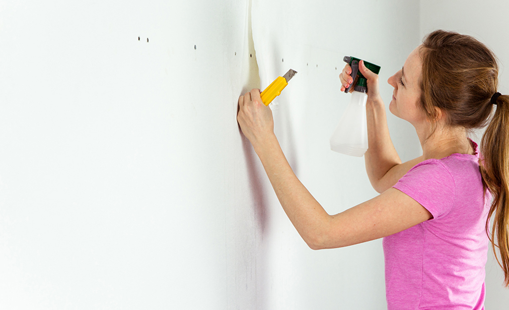 A person applies wallpaper remover with a spray bottle.