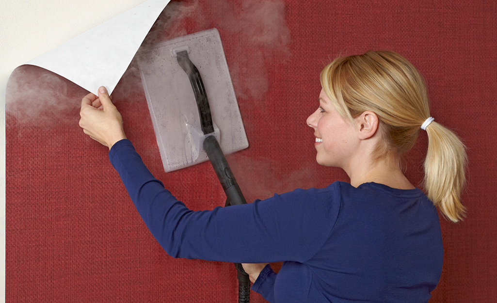 A person uses a steamer to remove wallpaper.