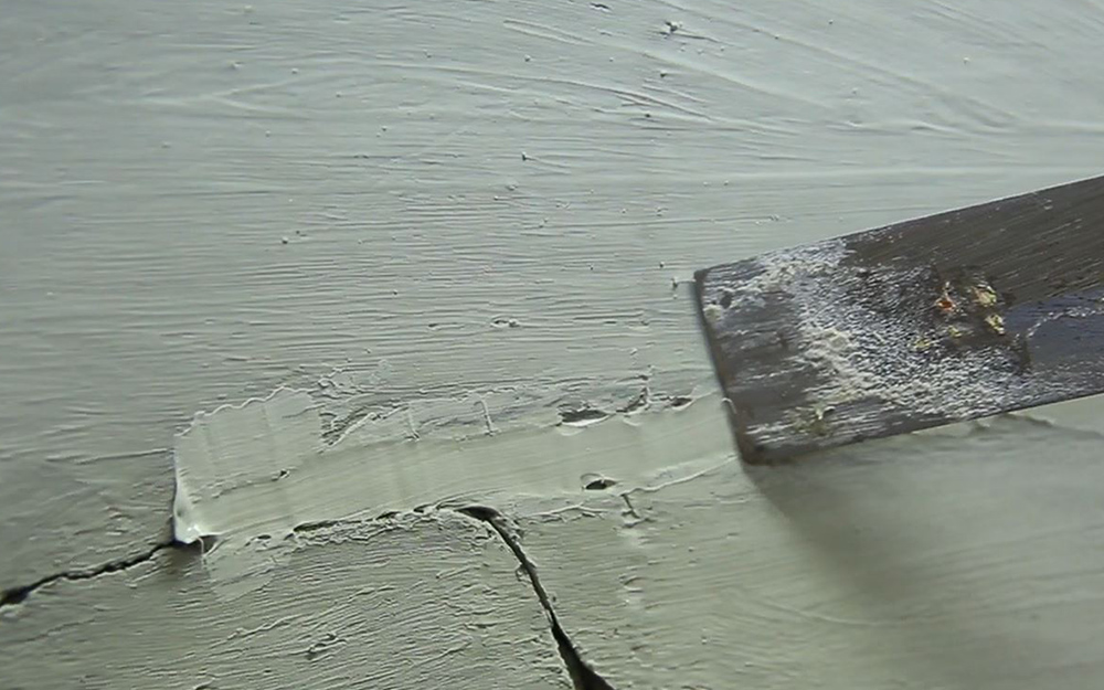 A putty knife smoothing filler over cracks in a concrete driveway.