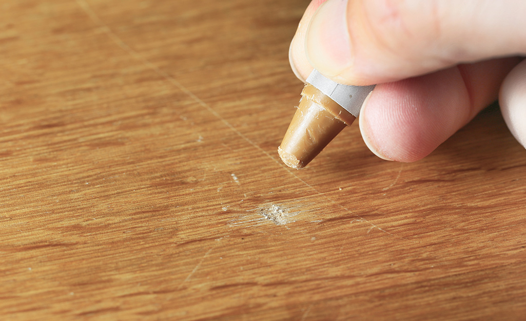 A person uses a crayon to fill in a scratch on laminate flooring.