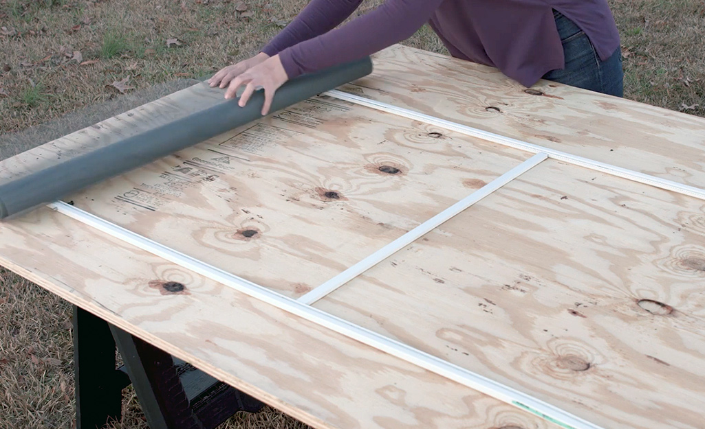 A person rolling new window screen mesh over the screen frame.