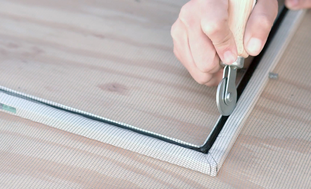 A person using a spline roller to secure a window screen spline into the screen frame.