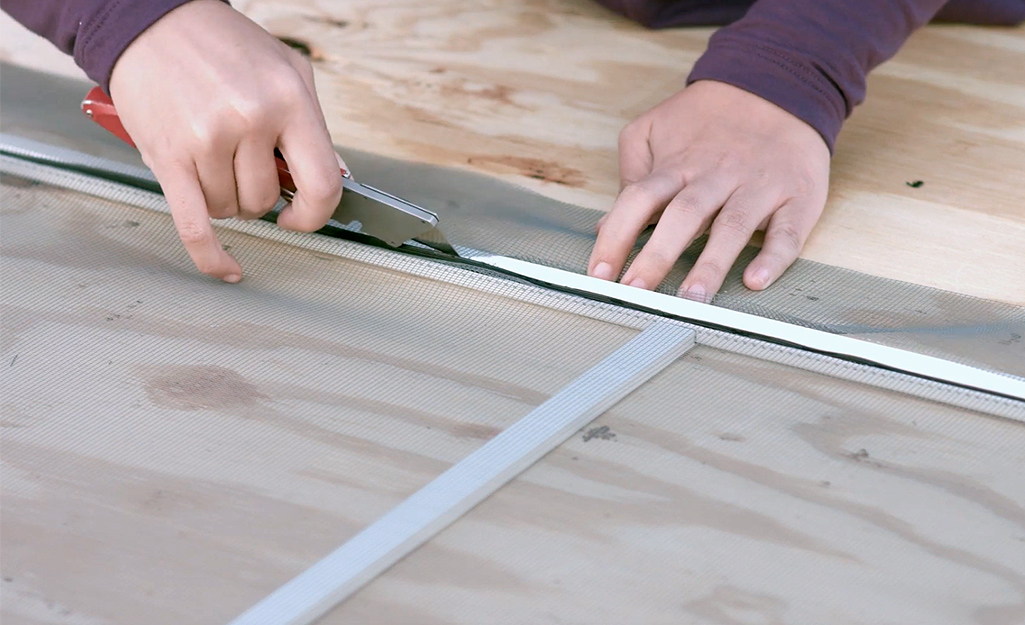 A person cutting away excess window screen mesh.