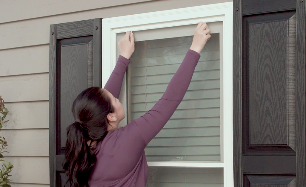 A woman replacing a window screen.