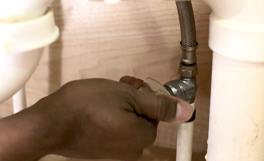 A person shuts off the water before replacing a bathroom faucet.