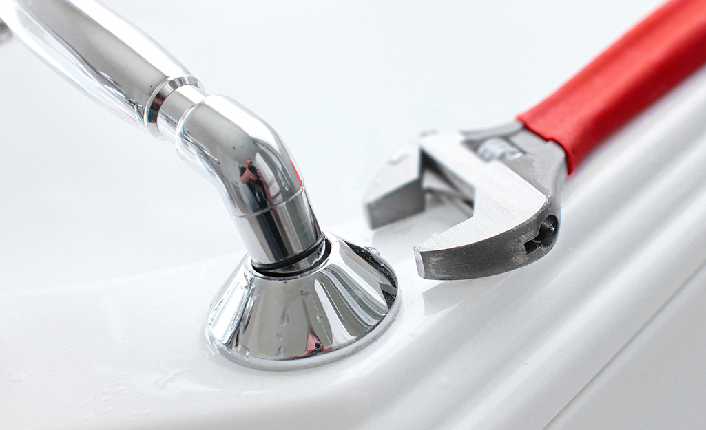 A person tightens a bathtub faucet spout in place with pliers.