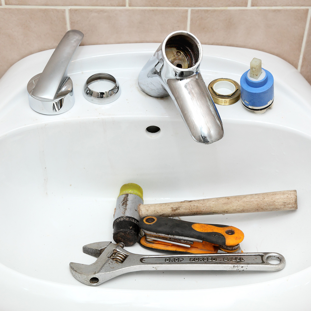 A bathroom cartridge faucet is disassembled with tools in the sink. A bathroom cartridge faucet is disassembled with tools in the sink.