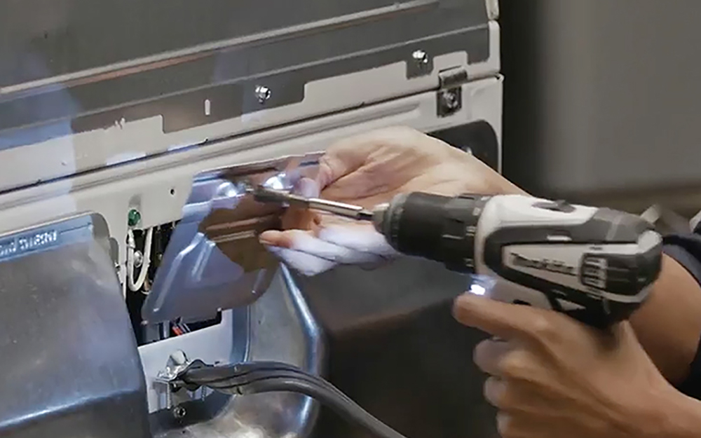 person using a drill to open a dryer access panel person using a drill to open a dryer access panel