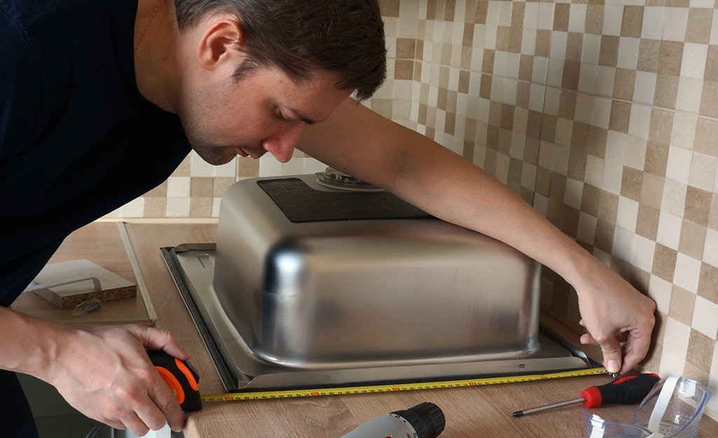 A person measuring a kitchen sink.