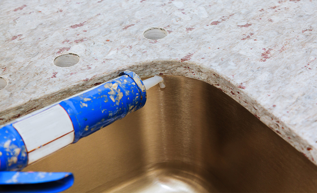 Someone adding caulk to a kitchen countertop and sink connection point.