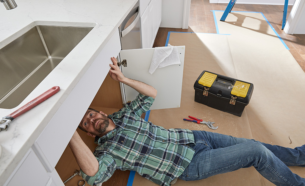 A man doing work under a kitchen sink. 