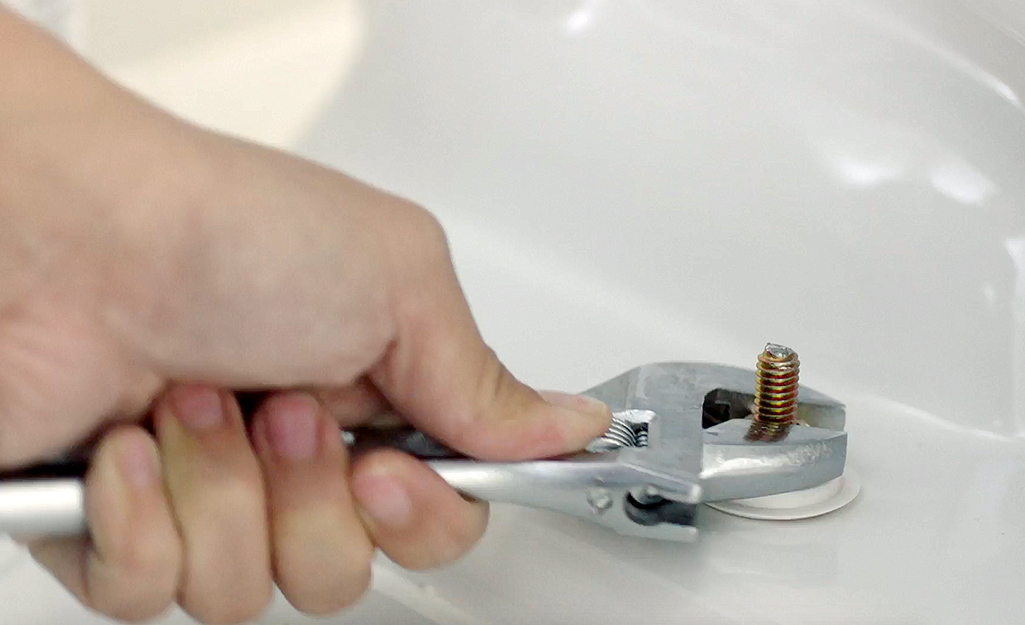 A person unscrewing a toilet bowl's mounting bolts.