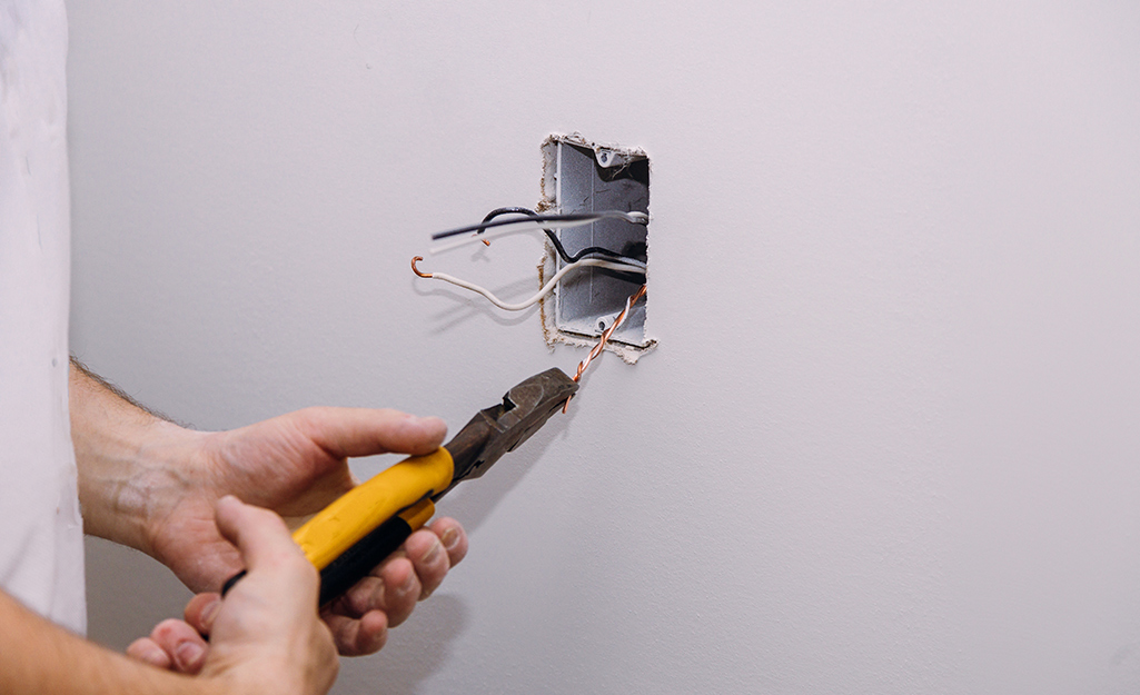 A person uses wire strippers to adjust the wiring of an outlet.