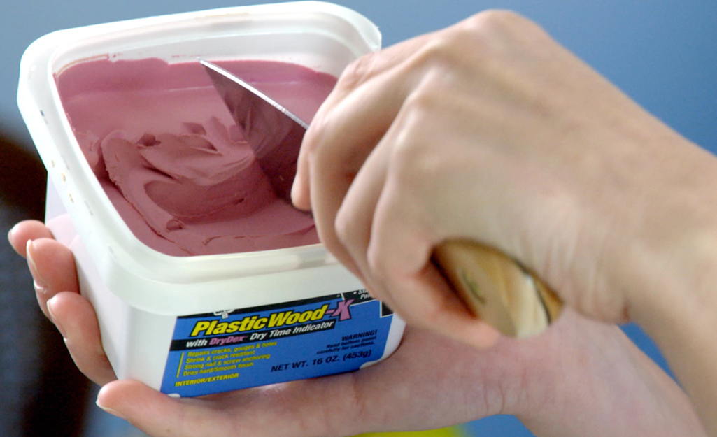 A person scooping up putty to patch a cabinet door.