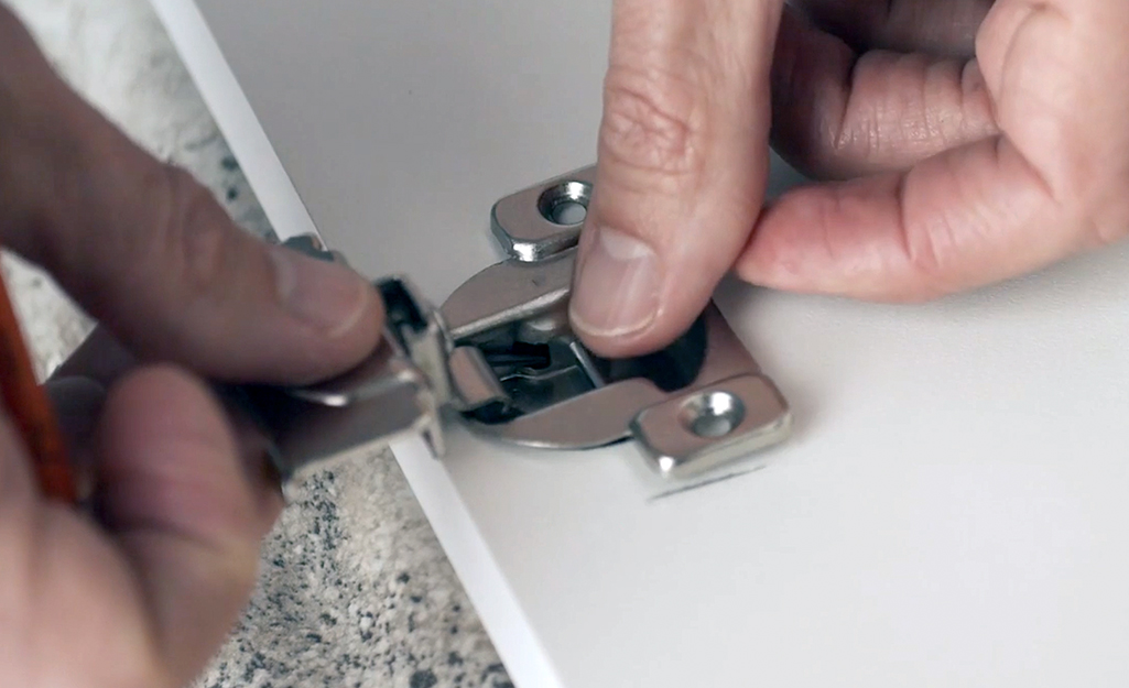 A person positioning new hinges to a cabinet door.