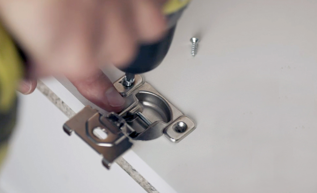 A person attaching a new hinge to a cabinet door with a drill driver.