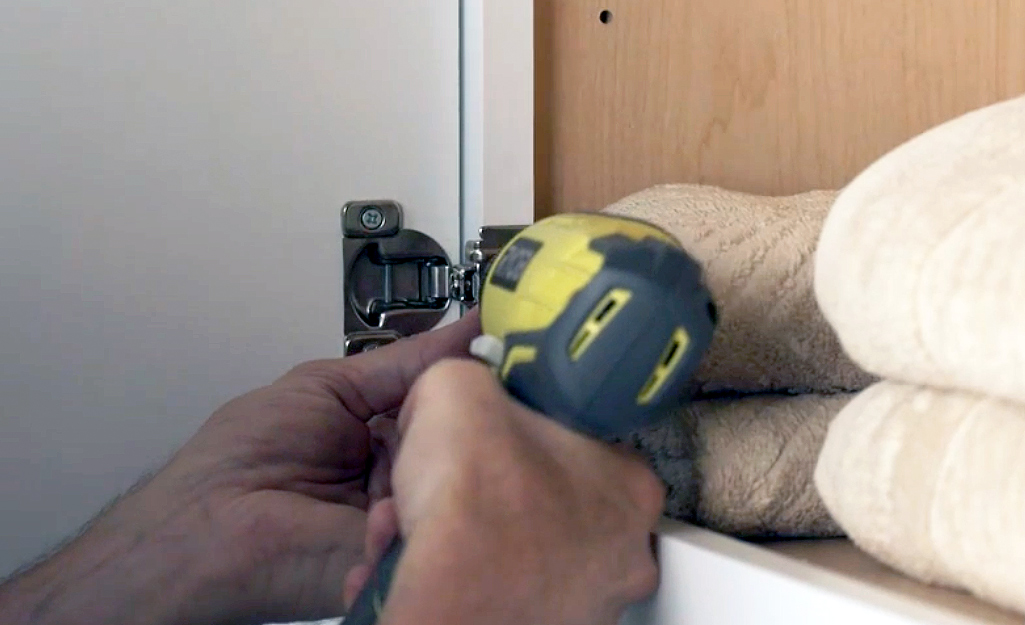 A person using a drill driver to attach a cabinet door.