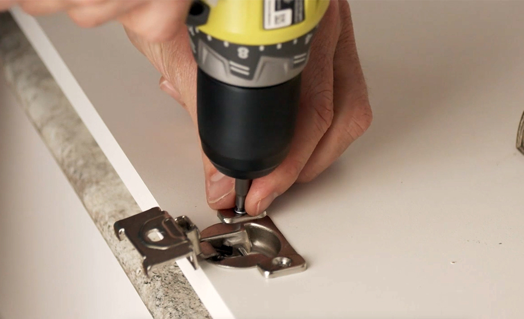 A person attaching a new hinge to a cabinet door with a drill driver.