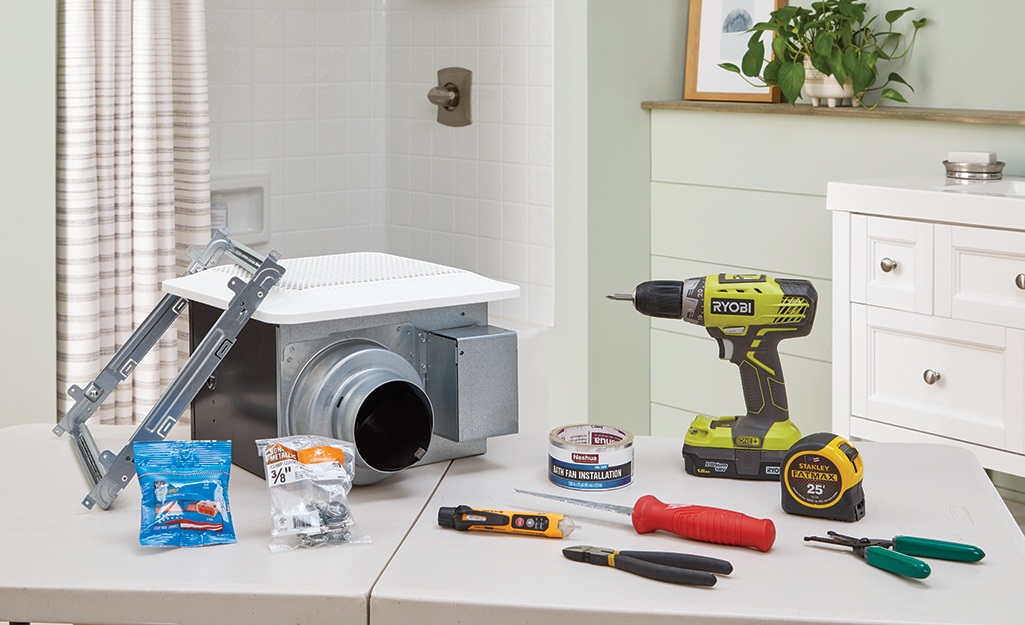 A bathroom exhaust fan sits on a table surrounded by the tools needed to install it.