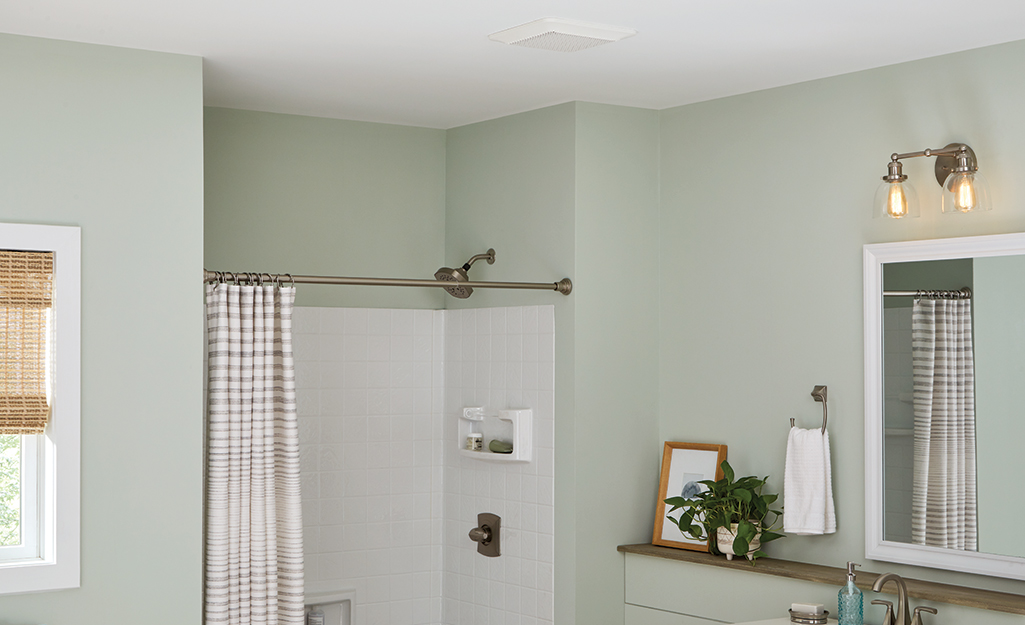 A shower stands in the alcove of a bathroom with an exhaust fan in the ceiling.