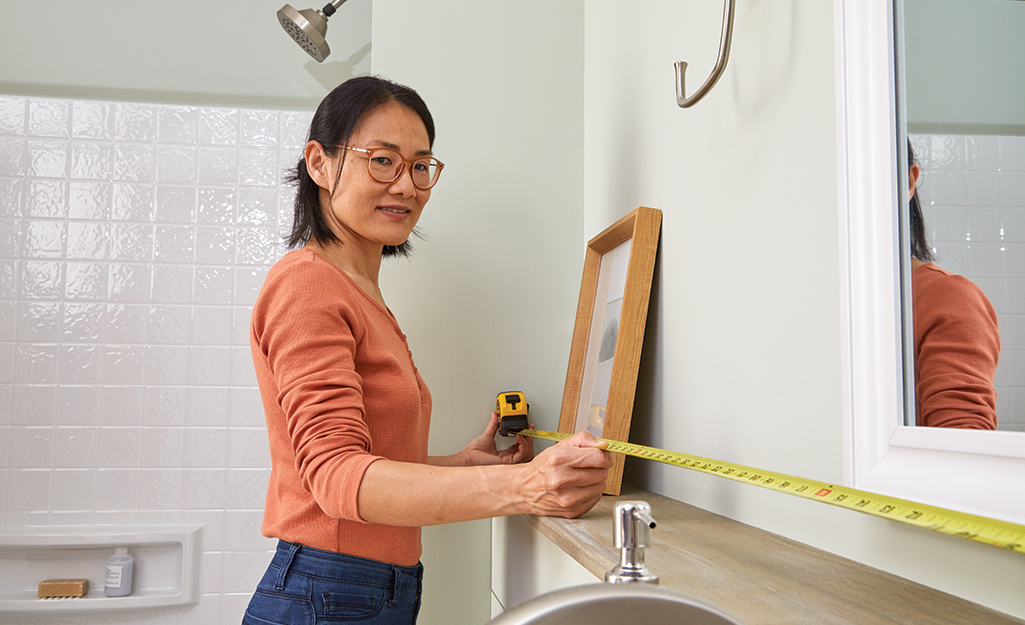 A woman stretches a tape measure along the wall of a bathroom.
