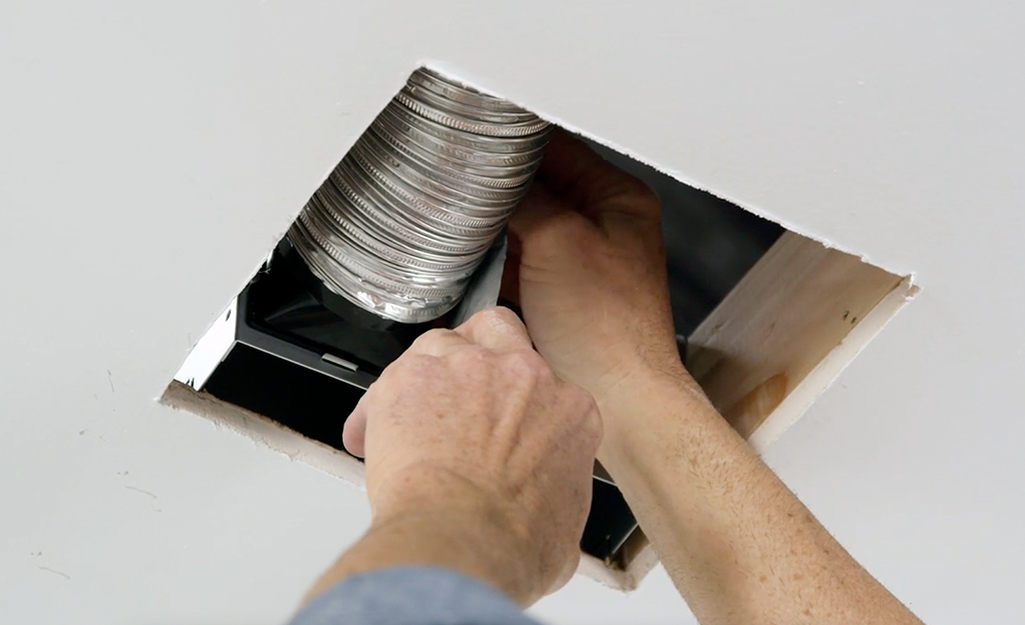 A person attaches the duct to a new bath fan. A person attaches the duct to a new bath fan.