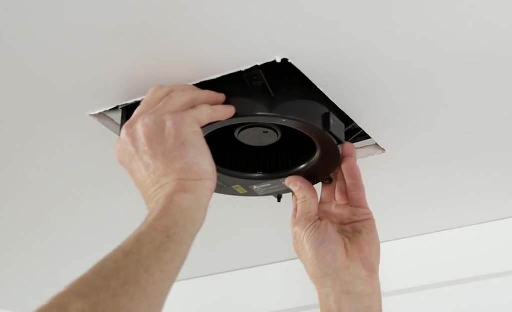 A person inserts fan housing into a bathroom ceiling.