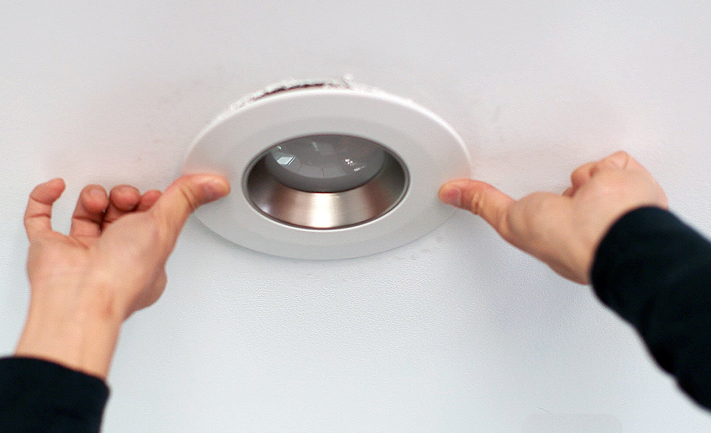 A person uses both hands to place a recessed lighting fixture into the ceiling.