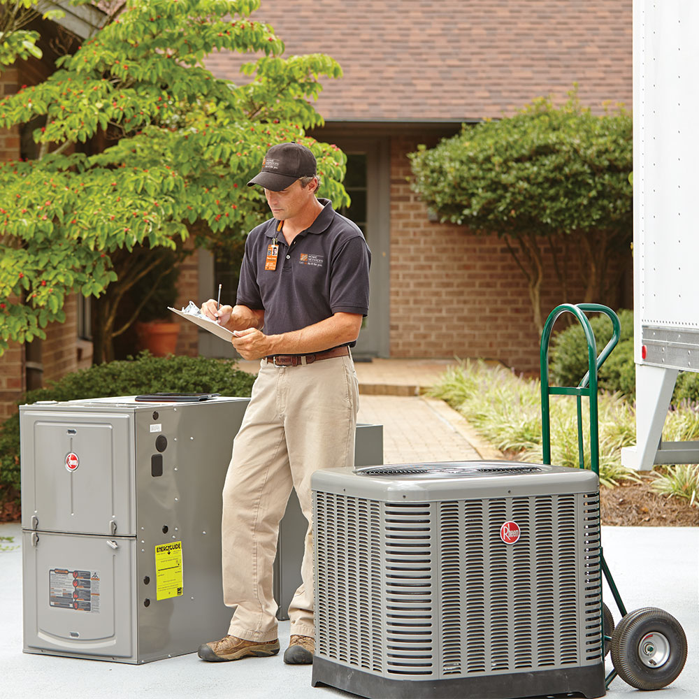 A Home Depot associate standing next to a new air conditioner and heater outside a home.
